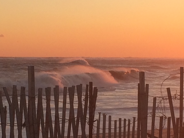 Photograph of the Atlantic Ocean, rough water and dune fencing during an orange sunset by Brenda Sinclair
